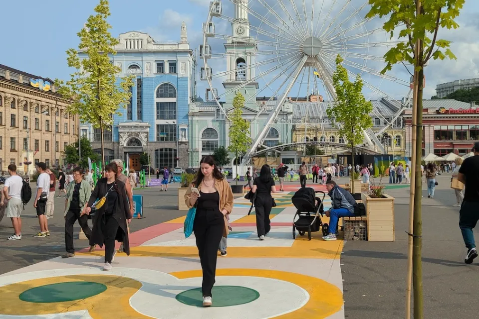 People walking in crowded square in Kyiv, Ukraine with ferris wheel and old buildings.